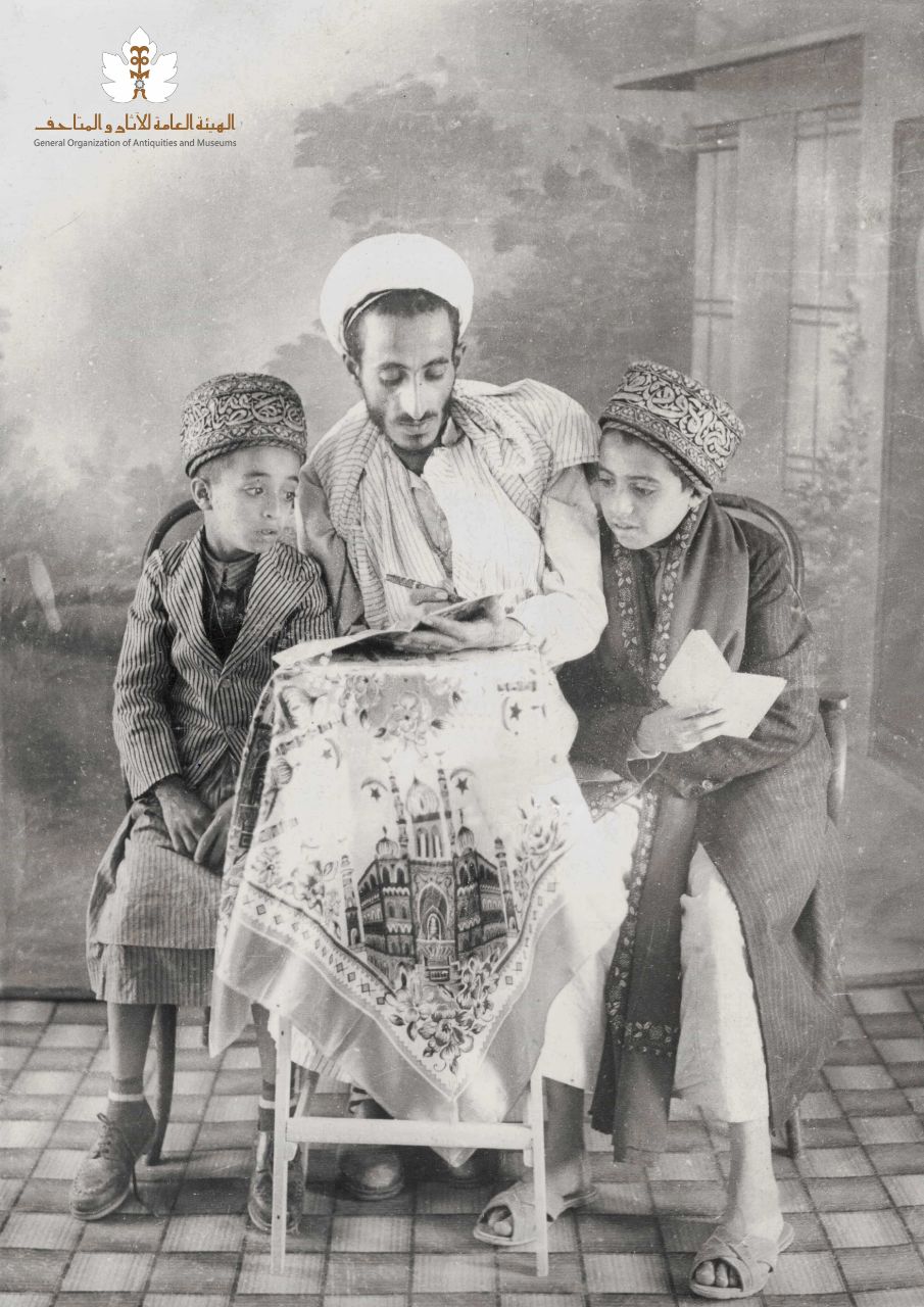 التاريخ: ١٩٥٩م تقريباً
الرقم المتحفي : 79fm
الوصف: صورة أخذت في أستوديو في صنعاء وفي الوسط الأستاذ محمد دلال وكان معروفاً بالعزي دلال وعلى يمينه السيد عبدالله بن محمد بن عبدالرحمن الشامي وعن يساره الأمير محمد بن المحسن بن يحيى حميدالدين.

 اسم المعرض : صور اليمن في حقبة المملكة المتوكلية - صورة رقم : 1